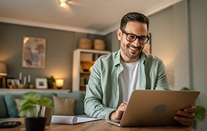 Man with glasses smiling while working on laptop at home