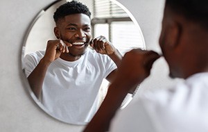 Patient smiling while flossing his teeth in bathroom