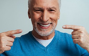 A handsome senior man gladly pointing to his new dentures