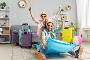 Young couple in living room, suitcases packed and celebrating on a pool floaty